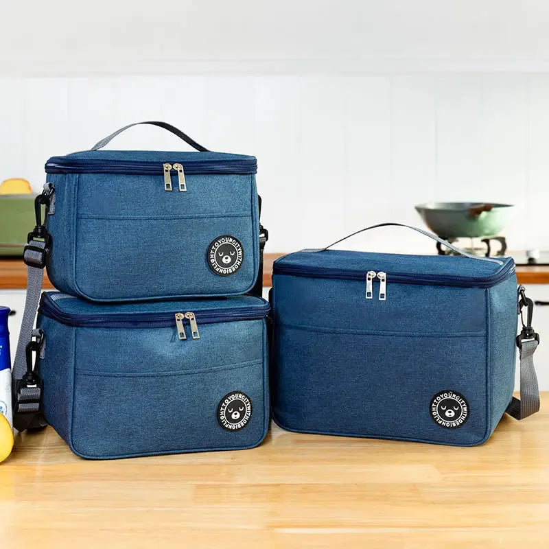 A navy blue insulated lunch bag with a shoulder strap is shown on a wooden surface.