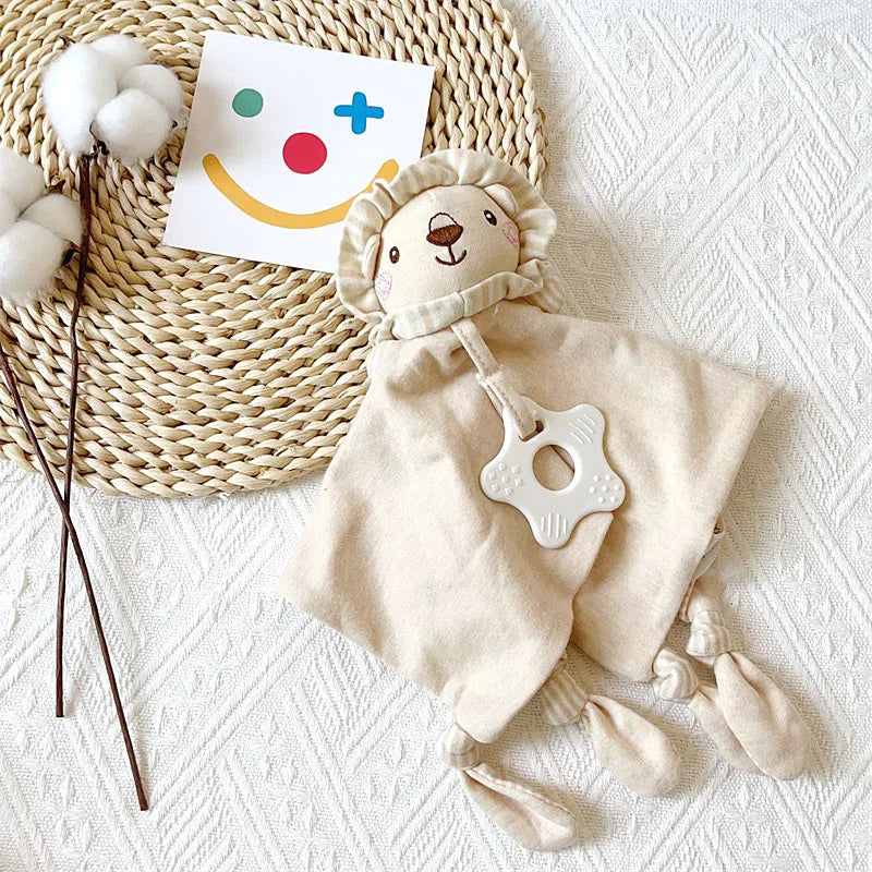 A beige elephant plush toy with a teether, rattle, and comfort blanket resting on a woven mat.
