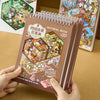 Braunes Spiralnotizbuch mit dem Titel Material Book, das eine Sammlung von Miniatur-Szene-Stickern zeigt.