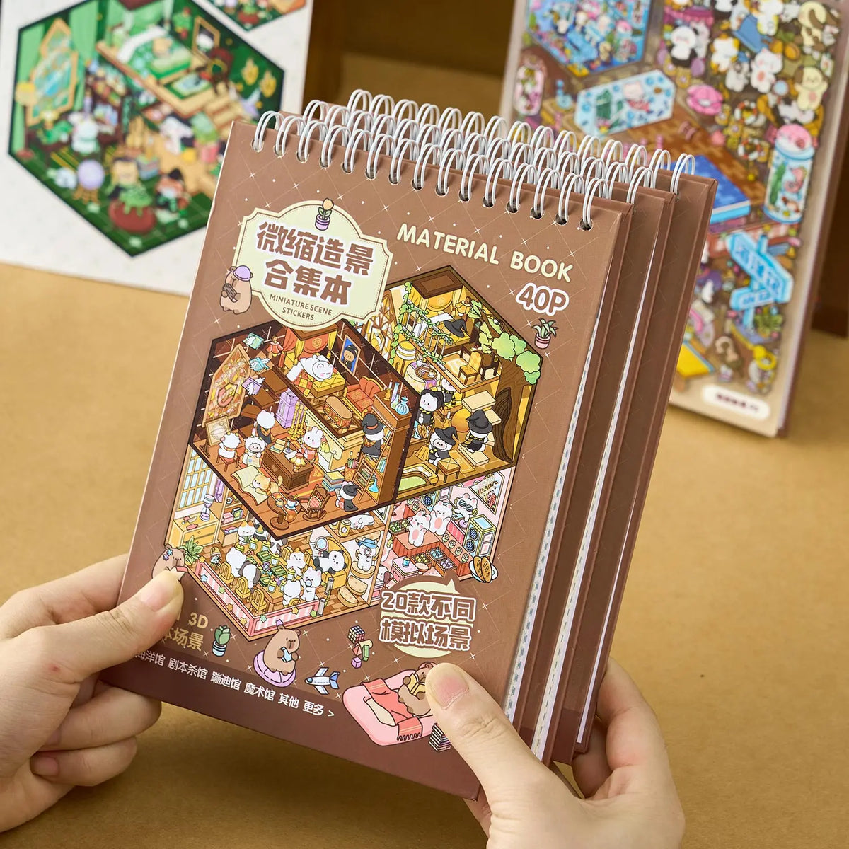 Braunes Spiralnotizbuch mit dem Titel Material Book, das eine Sammlung von Miniatur-Szene-Stickern zeigt.