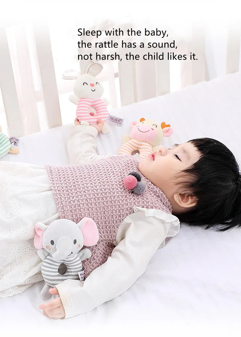 A baby is lying down and enjoying a soft plush rattle toy with a cartoon elephant design.