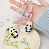 A hand holds a blind box panda figure and several beaded necklaces on a white plate.