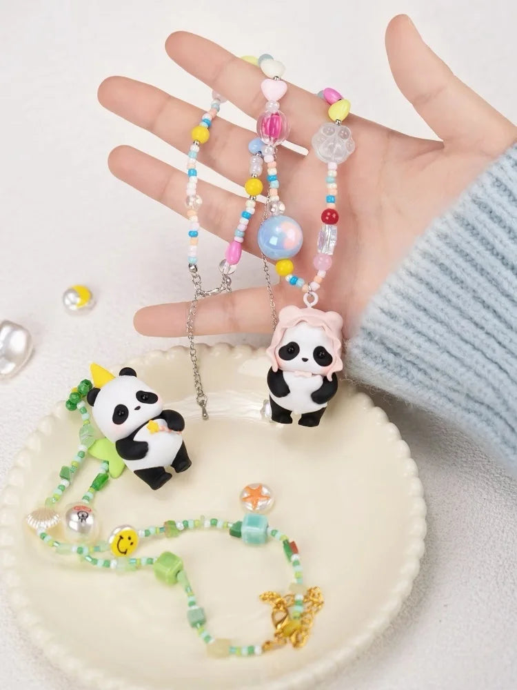 A hand holds a blind box panda figure and several beaded necklaces on a white plate.
