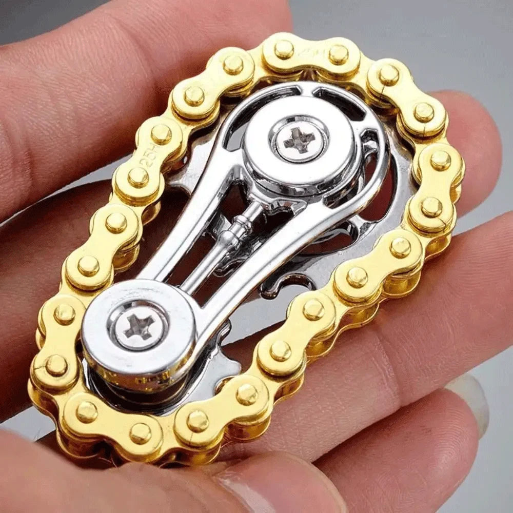 A hand holds a silver sprocket fidget spinner with a gold-colored, serrated ring design.