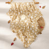 A beige muslin baby swaddle blanket with white polka dots is displayed on a light background.