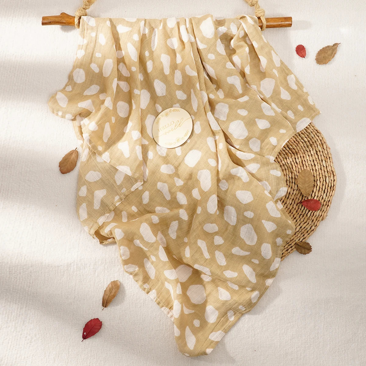 A beige muslin baby swaddle blanket with white polka dots is displayed on a light background.
