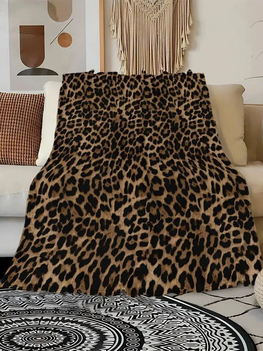 A close-up of a brown and black leopard print flannel throw blanket draped over a light-colored sofa.