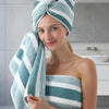 A woman smiling while holding a teal and white striped bath towel set.