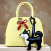 A yellow PU leather bag charm shaped like a black and white dog with a braided red bow.