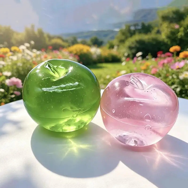 Two translucent fruit-shaped stress relief toys, one green and one pink, resting on a white surface outdoors.
