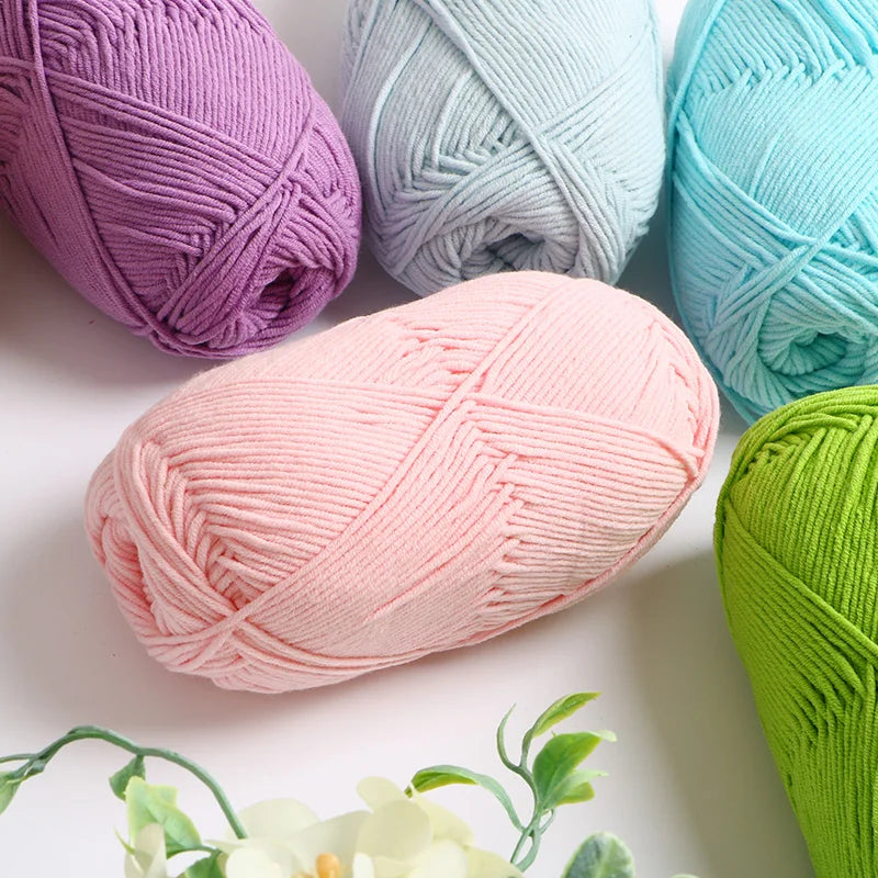 A collection of soft 4-ply milk cotton yarn in various shades of purple, blue, and pink, displayed on a white surface.