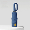 A blue compact folding umbrella with a handle is shown against a light gray background.
