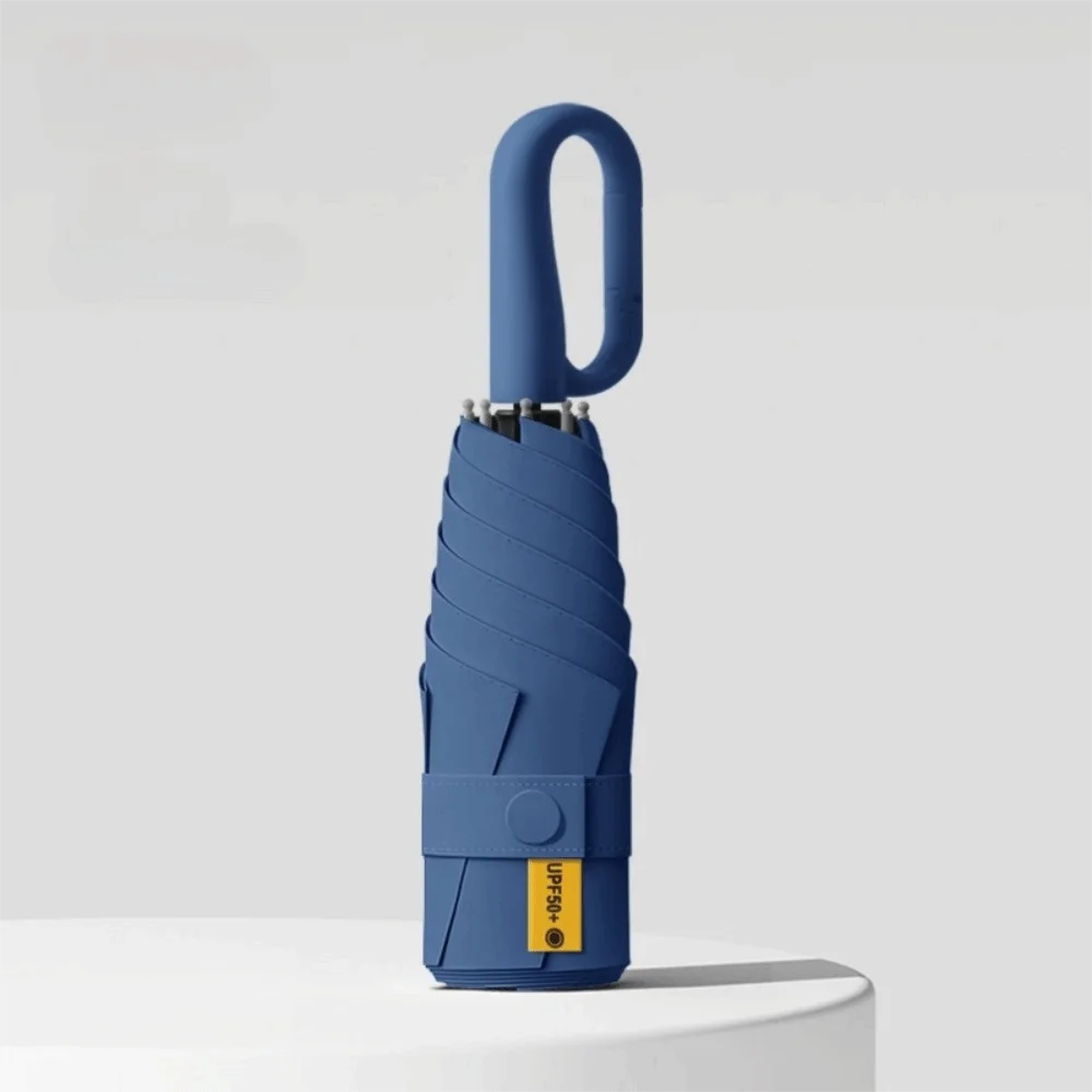 A blue compact folding umbrella with a handle is shown against a light gray background.