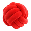 A round, red velvet throw pillow with a tightly knotted texture.