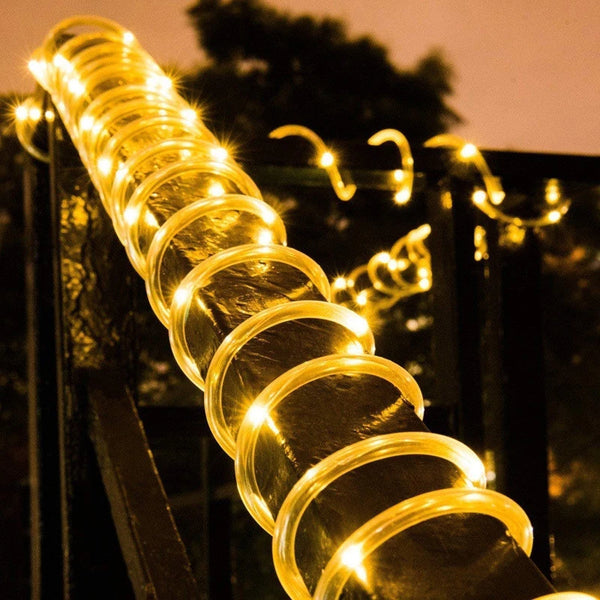 A close-up of a string of warm yellow LED lights coiled on a dark metal fence for outdoor garden decoration.
