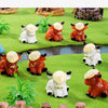 A collection of adorable resin Highland cow figurines in white and orange colors displayed on green mossy terrain.