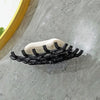 Wall-mounted soap dish with drainage featuring a white soap bar and black bristles mounted on a gray stone surface.