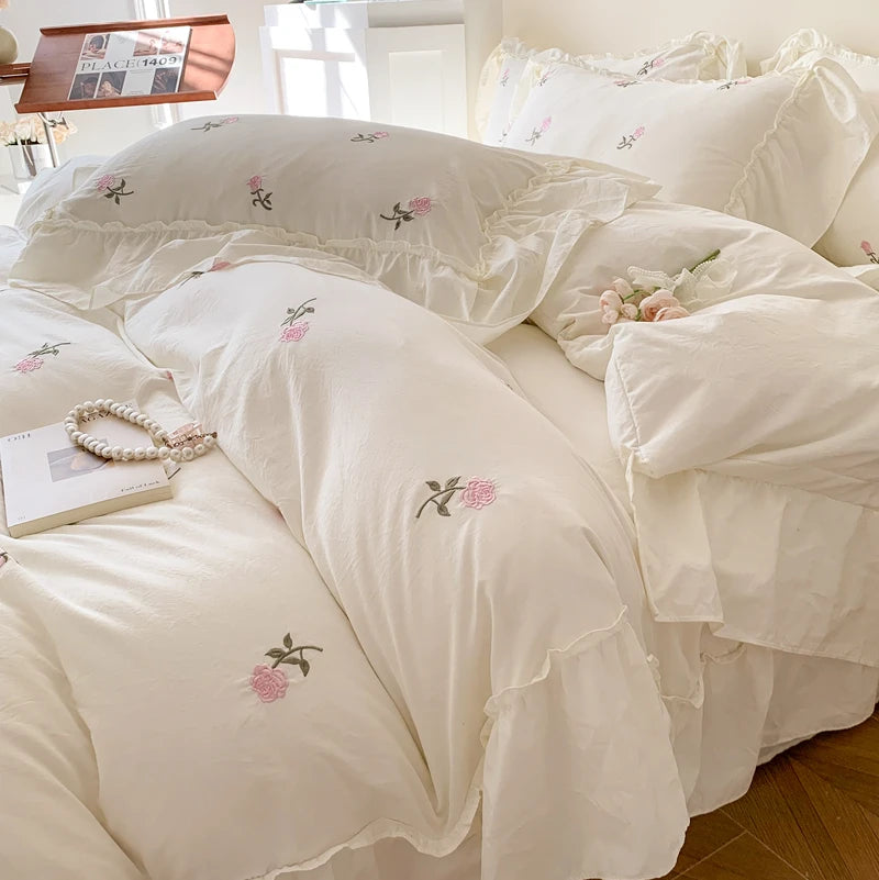 White duvet cover set with pink rose embroidery and lace details on a bed.