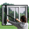 A person is installing a self-adhesive mosquito net window screen with a zipper on a white window frame.