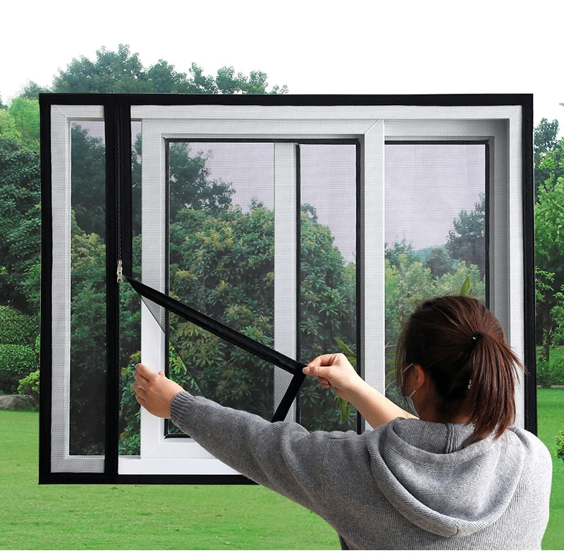 A person is installing a self-adhesive mosquito net window screen with a zipper on a white window frame.