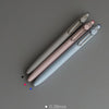 A collection of Uni ZENTO quick-dry gel pens in various sizes and colors laid diagonally on a gray surface.