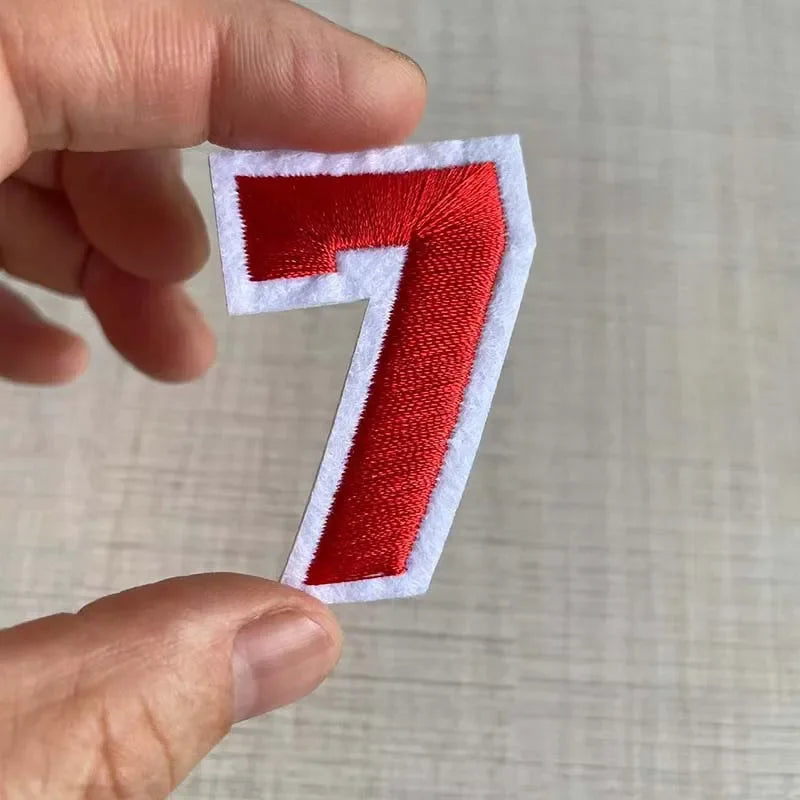 A hand holds a red embroidered number 7 patch on a white background.