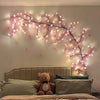 Pink cherry blossom string lights with flower vines illuminating a bedroom wall above a bed.