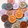 A collection of round, handmade PU leather labels in various pastel and earthy tones.