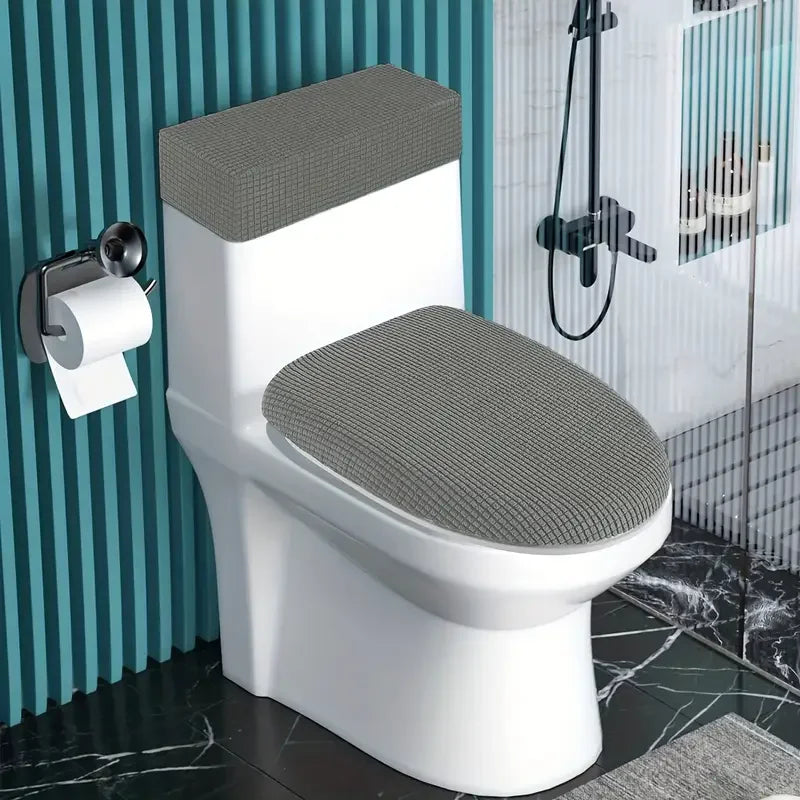 A white toilet with a gray fleece seat cover and matching lid and tank covers in a bathroom setting.