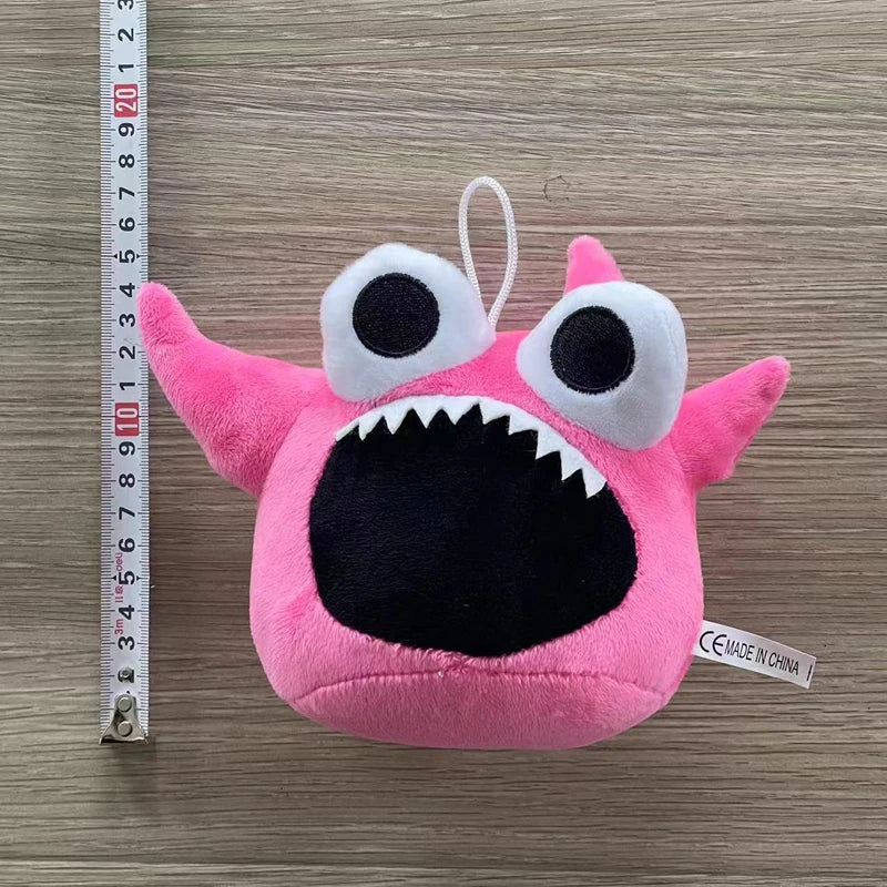 Pink plush toy of Opila Bird with large eyes and a wide mouth, measured against a ruler.