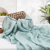 Light mint green muslin baby swaddle blanket draped on a white surface with a woven basket in the background.