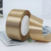 A roll of luxurious satin ribbon in a golden beige color is shown next to a piece of paper.