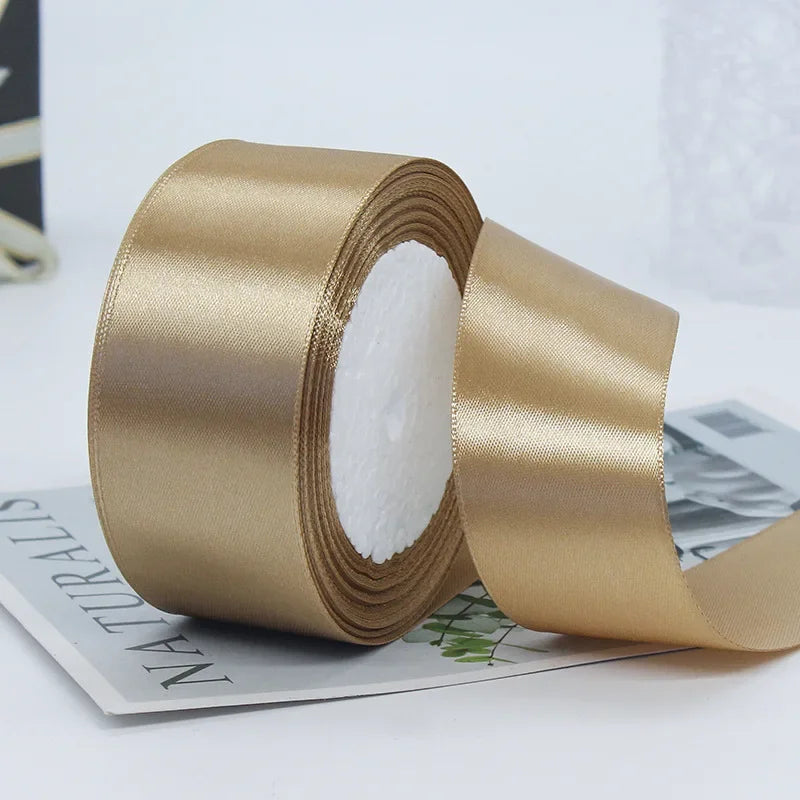 A roll of luxurious satin ribbon in a golden beige color is shown next to a piece of paper.