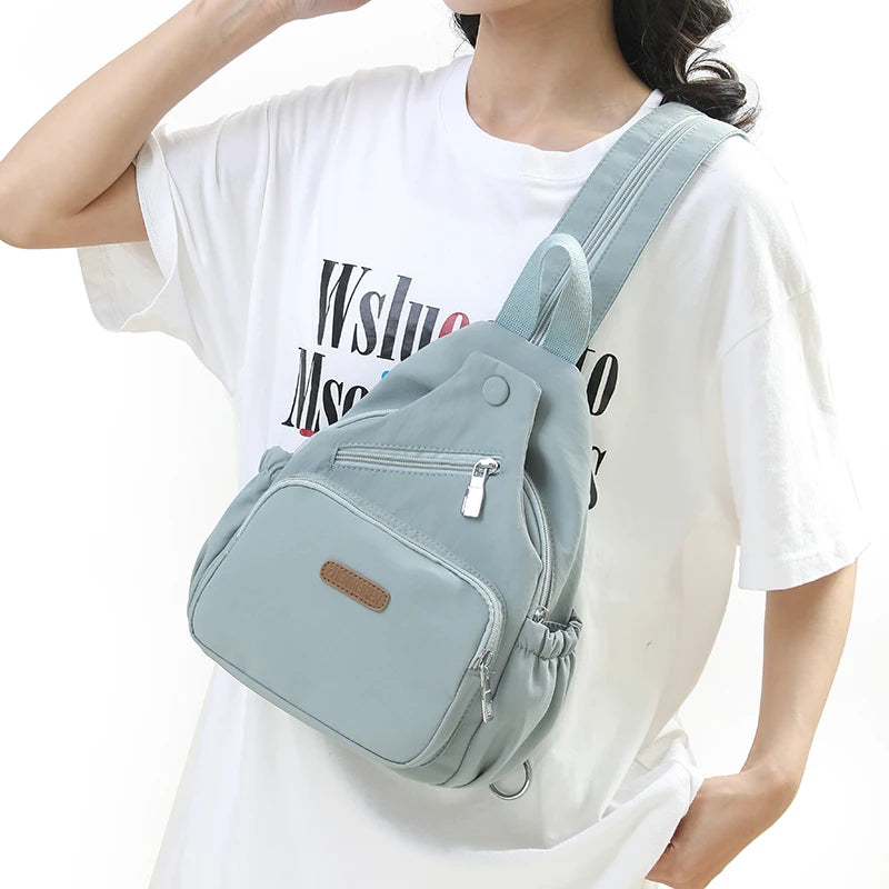 A light blue waterproof nylon crossbody sling bag worn by a woman, featuring a flap closure and strap.