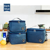 Two dark blue thermal insulated lunch bags with adjustable shoulder straps resting on a wooden surface.