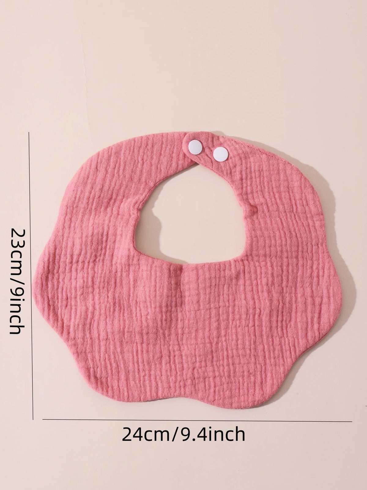 A pink soft cotton baby bib with a ruffle trim is shown against a light background.