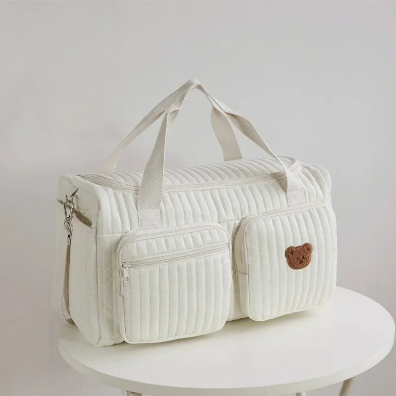 A white embroidered cotton diaper bag featuring a bear design on the front, shown on a white surface.