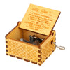 A vintage hand-cranked wooden music box with a lid open, featuring engraved text and a metal crank.