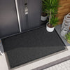 A black non-slip doormat with a hexagonal pattern placed outside a dark gray door.