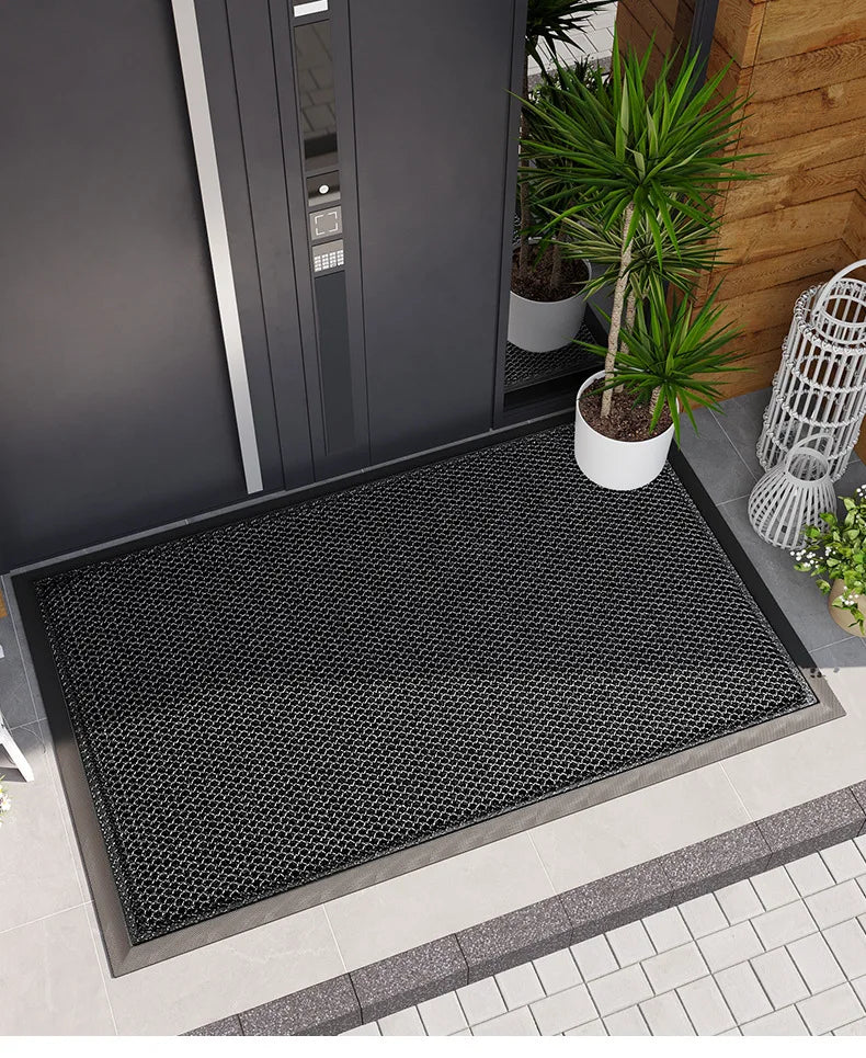 A black non-slip doormat with a hexagonal pattern placed outside a dark gray door.