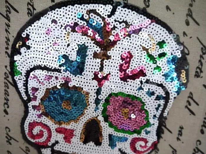 A white skull embroidered patch made of iridescent sequins and colorful thread for DIY clothing.