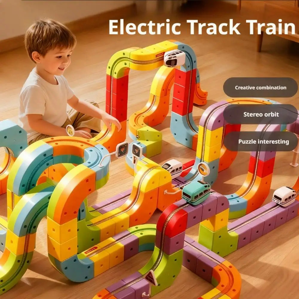 A child is playing with a colorful electric track train set made of interlocking blocks on a wooden floor.