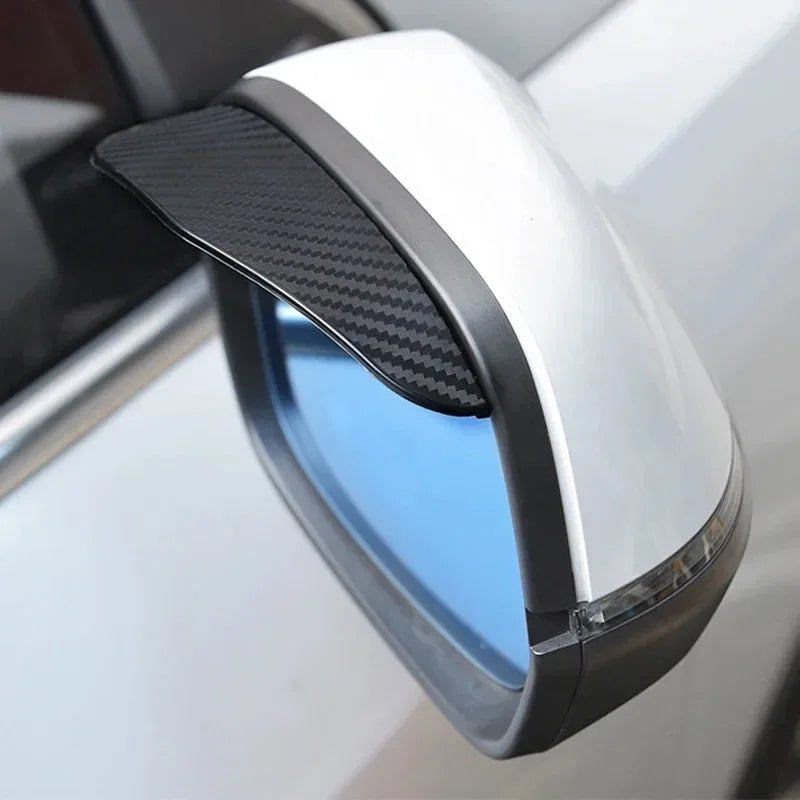 A close-up view of a car side mirror with a black carbon fiber rain and sun visor attached.