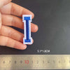 A hand holds a blue embroidered letter I patch, measuring 5.1 by 1.8 cm against a ruler.