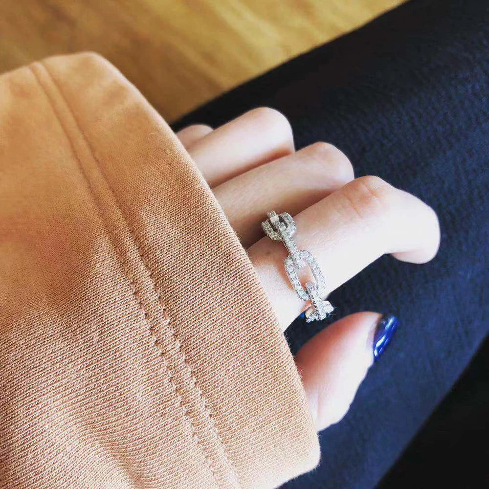 A hand wearing a geometric sterling silver stackable ring with cubic zirconia on a dark fabric background.