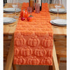 Orange pumpkin and ghost themed table runner set on a wooden table with plates and glassware.