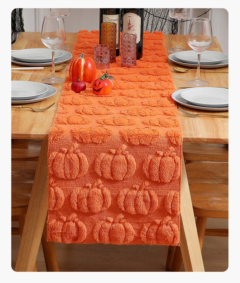 Orange pumpkin and ghost themed table runner set on a wooden table with plates and glassware.
