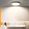 A hand holds a remote control while a person relaxes in a bathtub under an LED ceiling light.