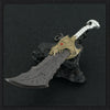A detailed metal sword with a gold hilt and dark blade rests on a black rock, featuring an ornamental design.