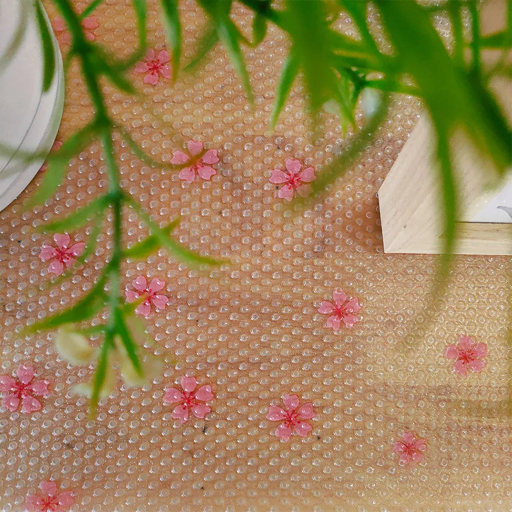 A close-up of a light pink cabinet liner with small, raised dots and green foliage resting on the surface.